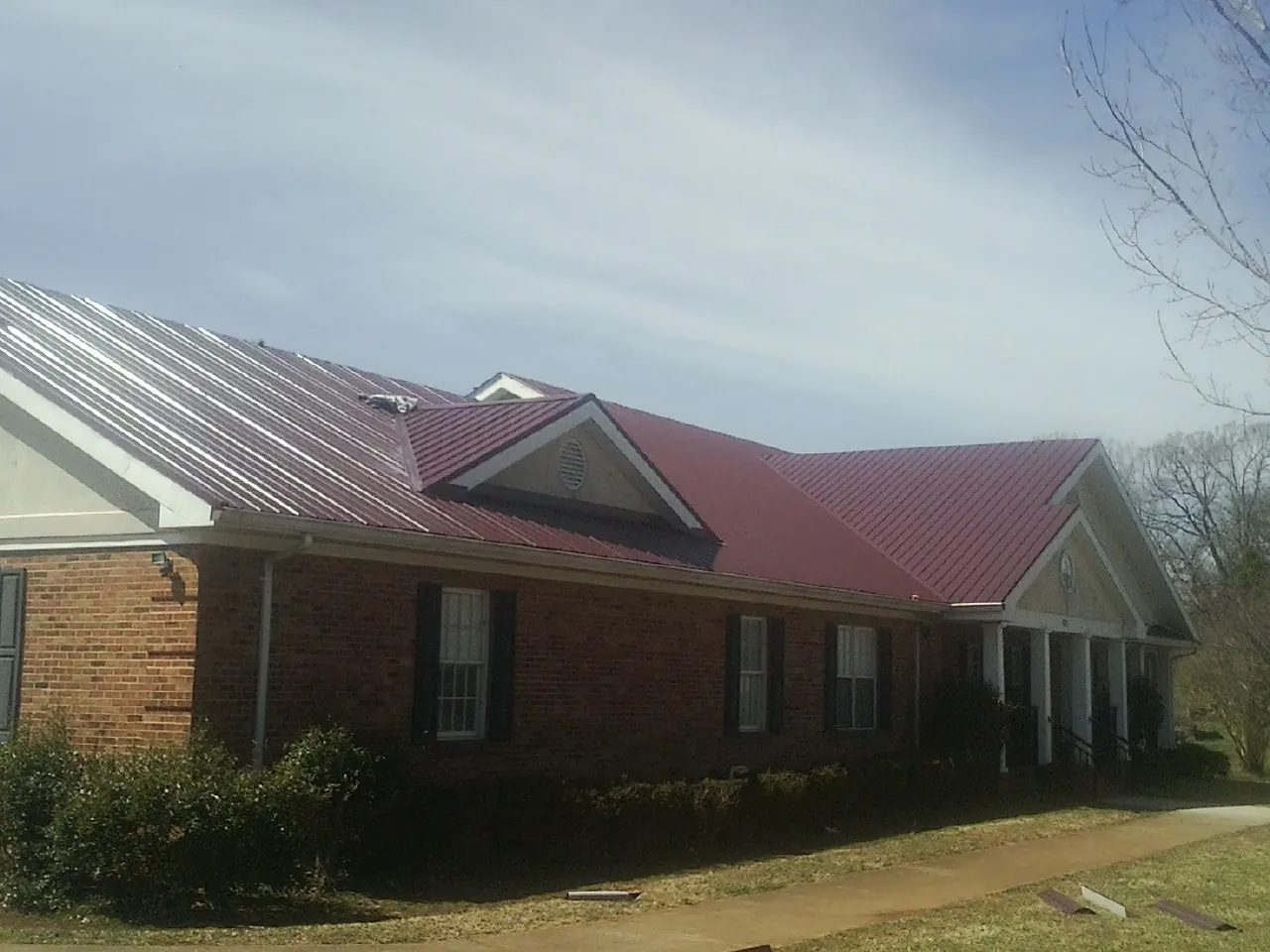 Red metal roof with gabled entries on a long brick building, from a Hail Damage Roof Repair job in Coulee Dam