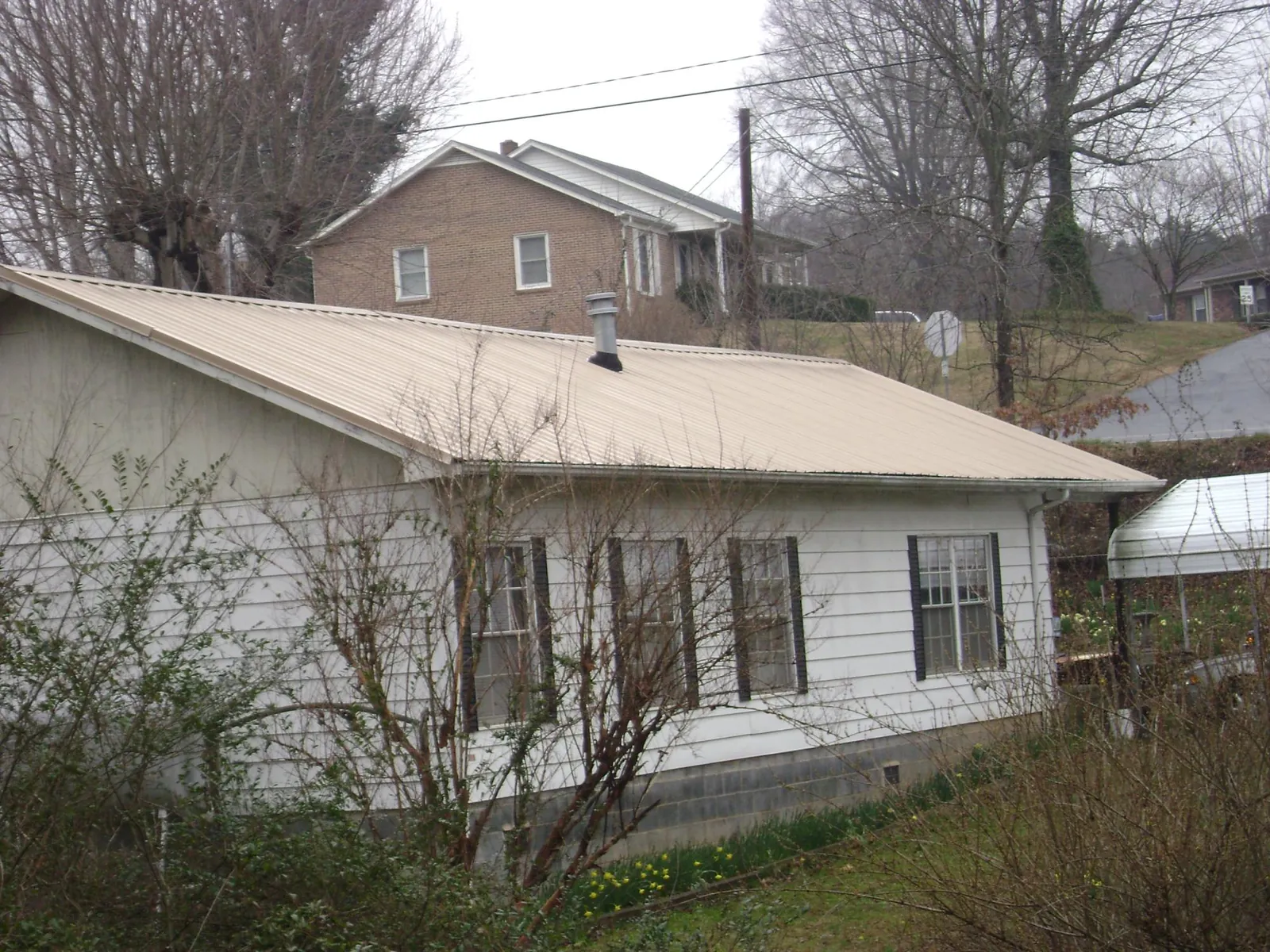 Tan metal roof on a white sided house set into a hillside — Commercial Roofing by Roofing Brothers in Coulee Dam
